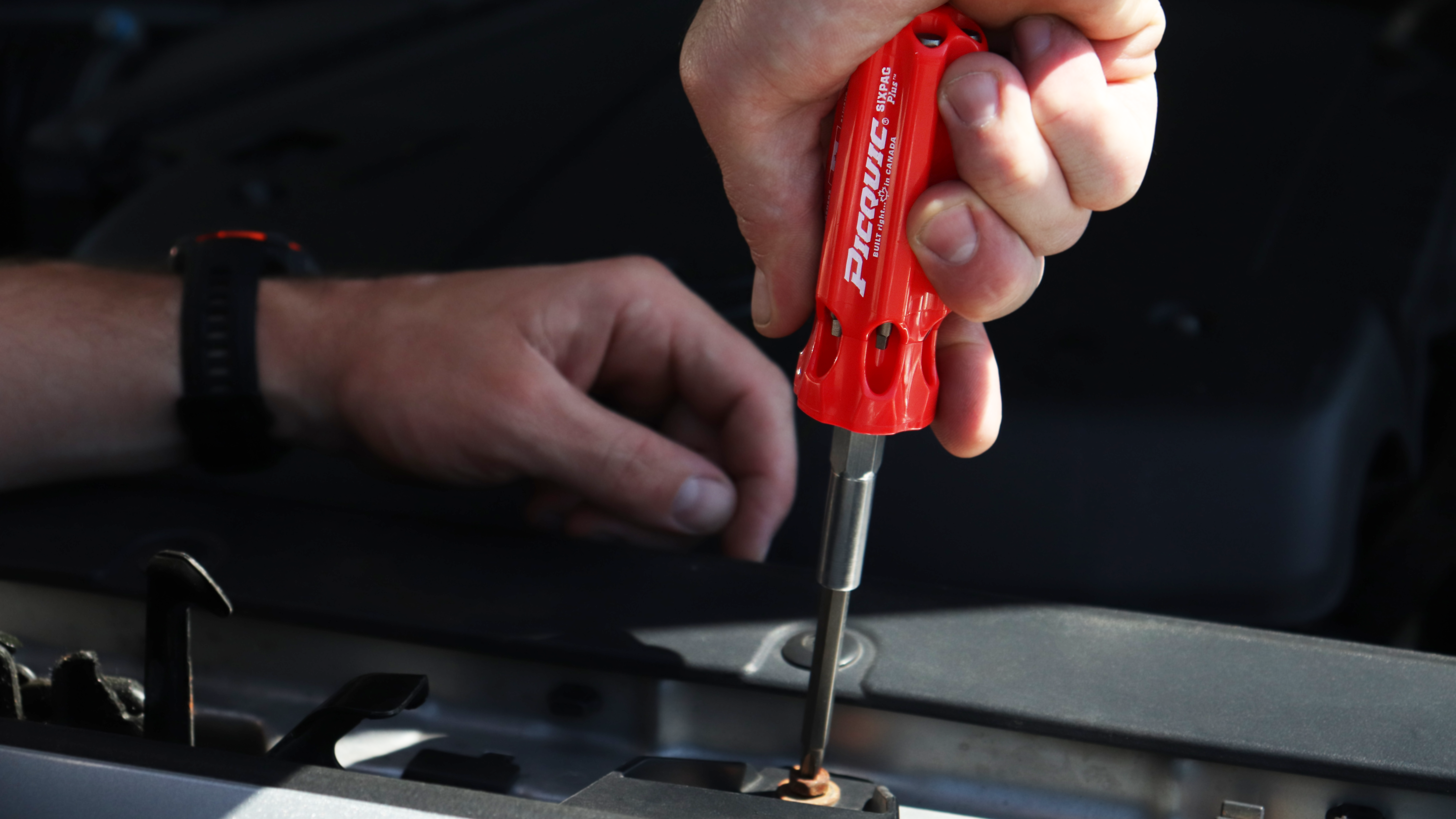 Person using a red screwdriver to work on a car engine.