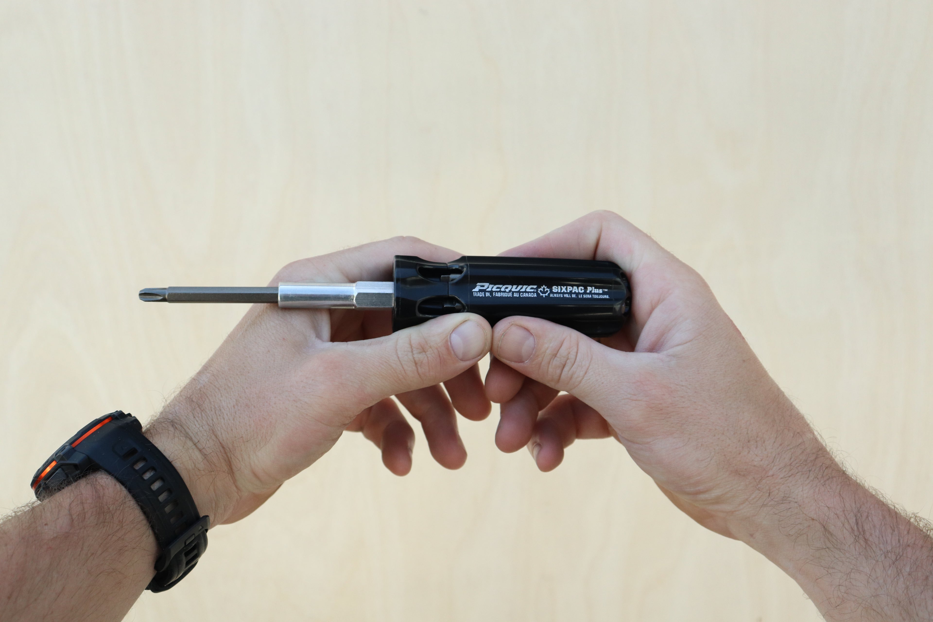 Person holding a small black tool with a metallic component against a beige background